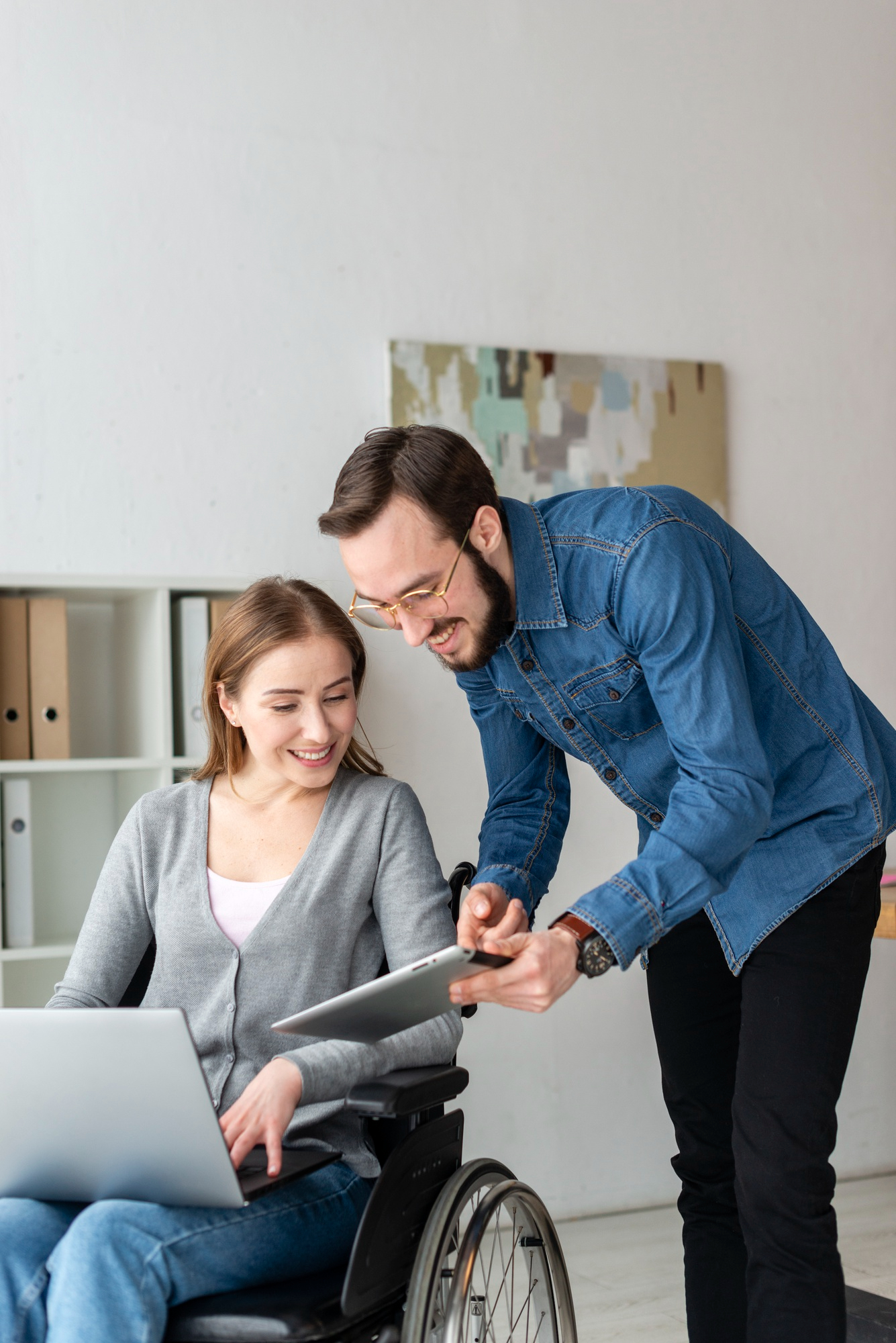 A woman in a wheelchair collaborates with a man using a laptop, engaged in a discussion or project together.