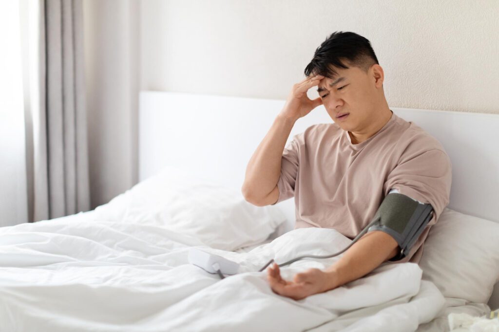 Man in pajamas sitting in bed at home checking blood pressure