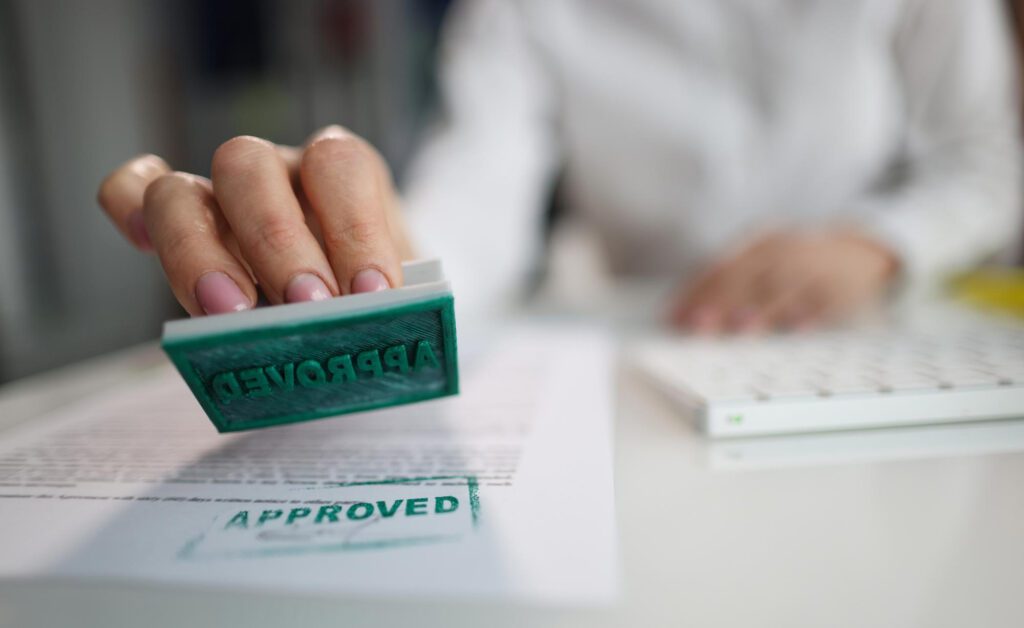 Manager hand putting stamp approved on document in office closeup
