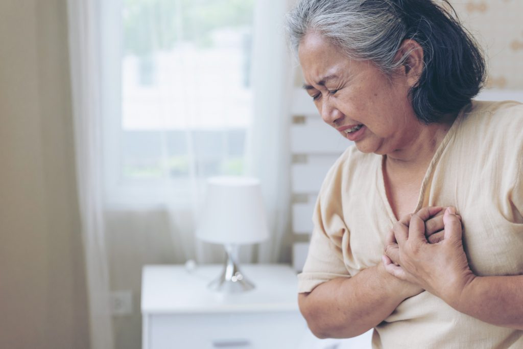 An elderly woman holding her chest in distress, indicating pain.